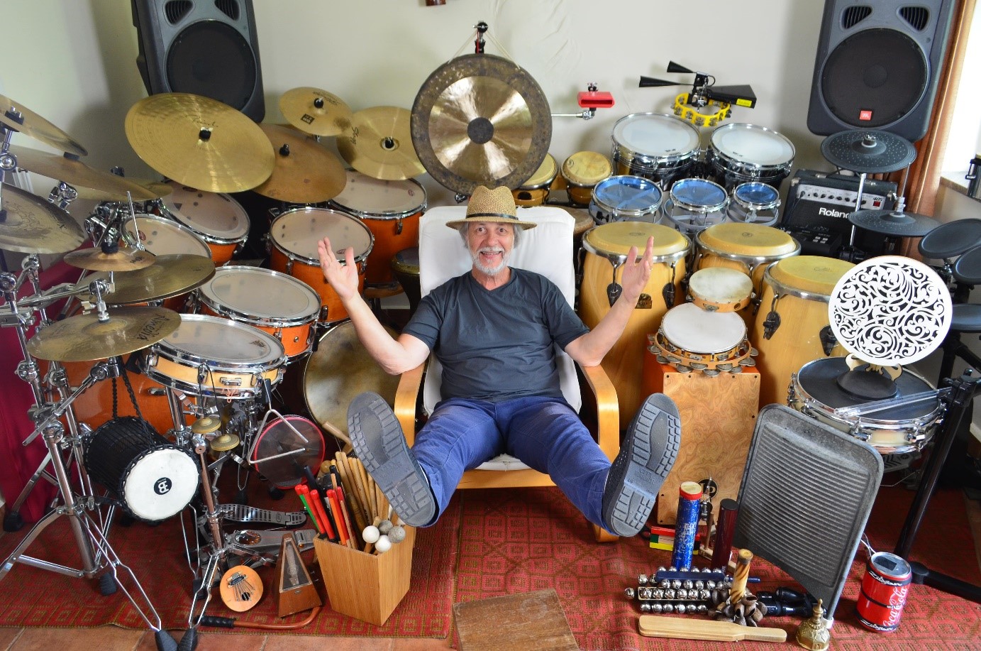 Obraz przedstawiający rozłożone instrumenty na całej szerokości pokoju: zestawy perkusyjne, kongi, talerze, rototomy, cajon i wiele innych.

Na środku jest uradowany prowadzący z rozłożonymi nogami w powietrzu.
